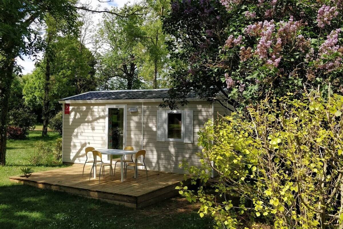 Een klein, gelijkvloers huisje met een terras en een tafel met stoelen.