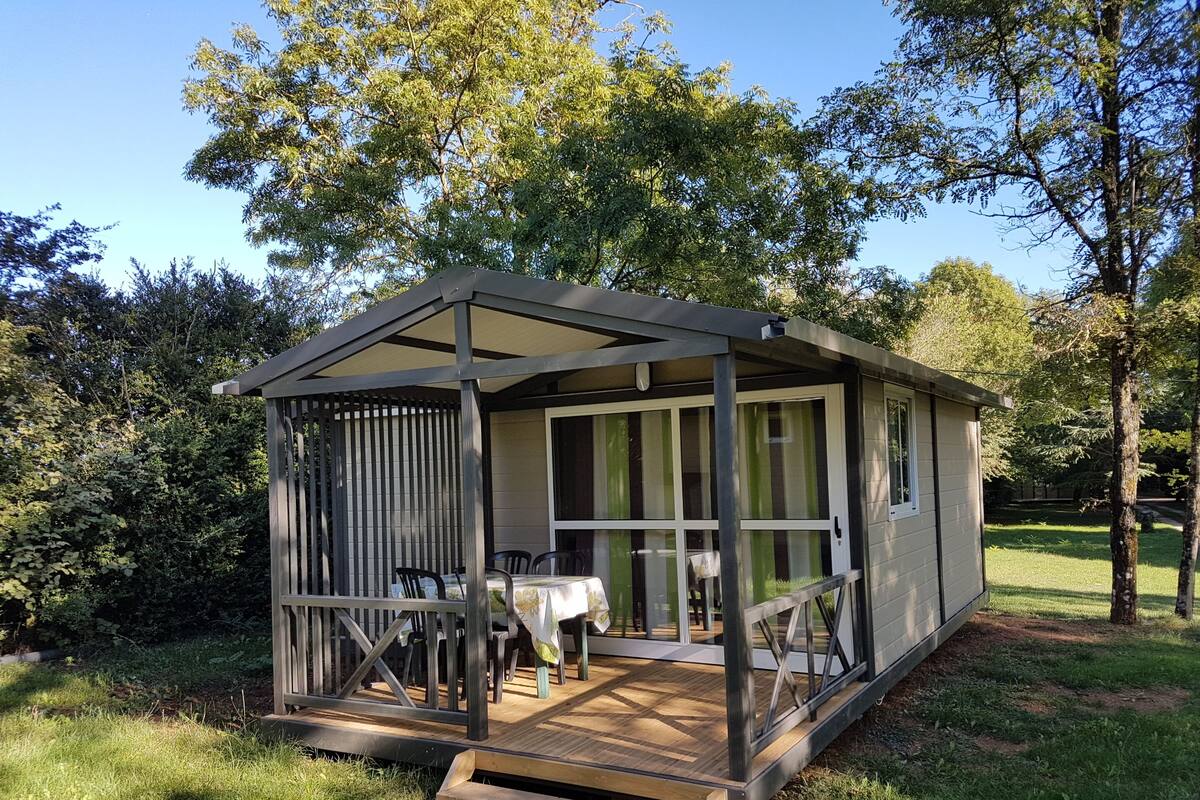 Een klein houten gebouw met één verdieping, een veranda, een tafel en stoelen.