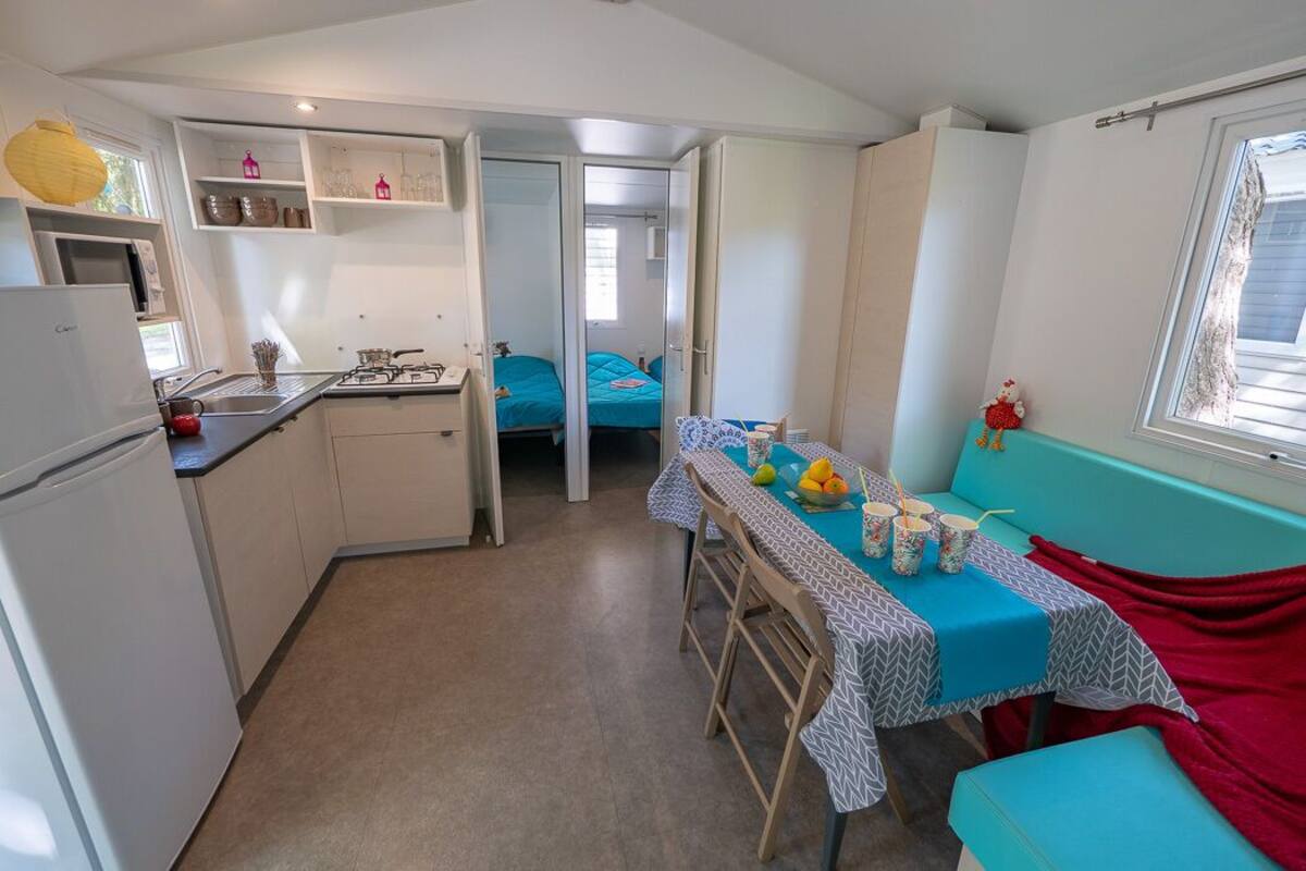 Een compacte keuken met een koelkast, wastafel en een eethoek met een tafel gedekt voor twee personen.