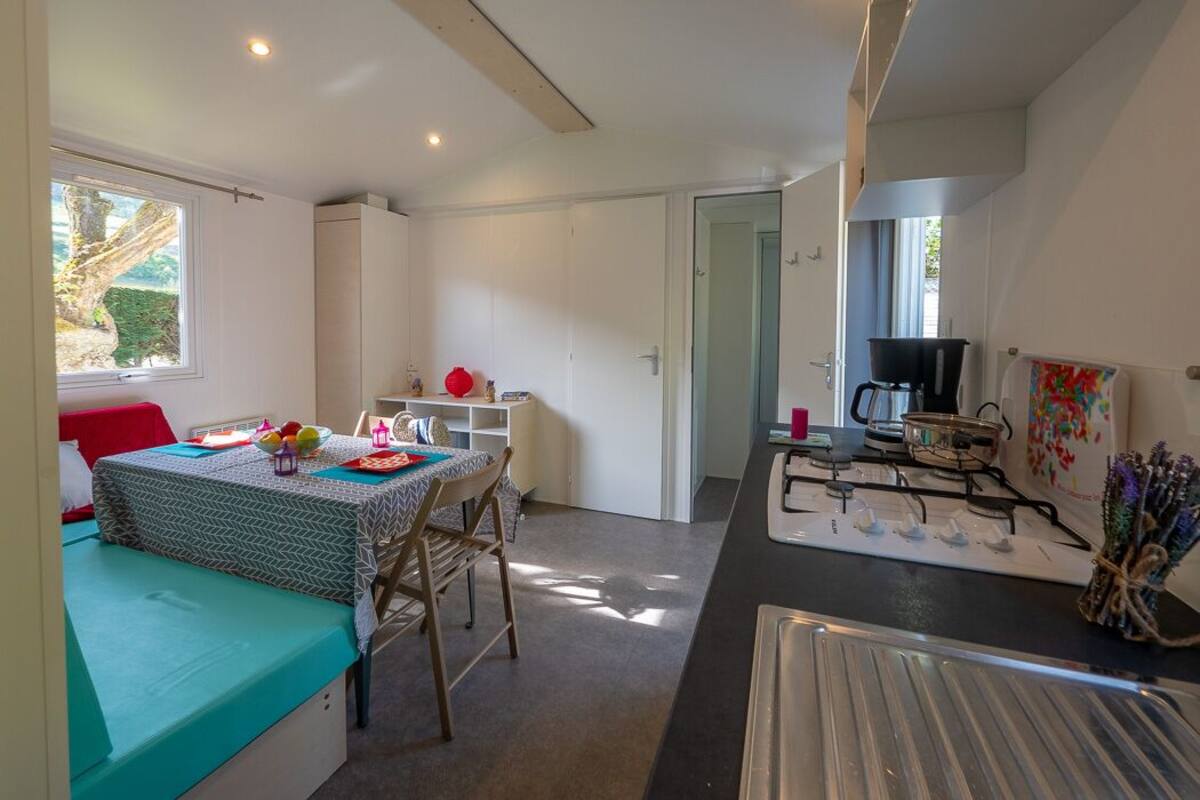 Een ruimtelijk ingerichte leefruimte met kitchenette, een eethoek en een bed.
