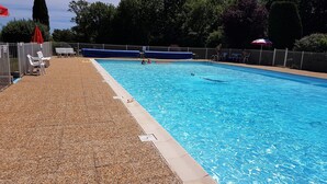 A swimming pool with a pebble-lined deck, a lifeguard stand, and a fenced area with lounge chairs and umbrellas. - Au Tour De L'Aveyron (L'Hospitalet-du-Larzac)