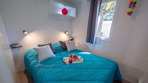A bedroom with a teal bedspread, a small shelf with a red lantern, and a window with curtains. - Au Tour De L'Aveyron (L'Hospitalet-du-Larzac)