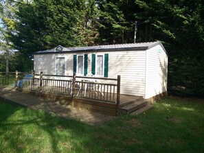 Une petite cabane à un seul étage, dotée d’une terrasse entourée d’une clôture et d’un espace extérieur aménagé avec des sièges.
