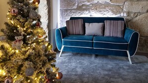 Un salón acogedor con un sofá de terciopelo azul, un árbol de Navidad decorado y tres cuadros en la pared.