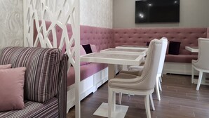 Un área de descanso moderna con un sofá rosa, un sillón a rayas y mesas blancas.