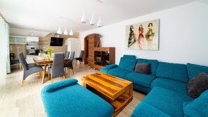 Een moderne woonkamer met een turquoise bank, een houten salontafel, en een eetgedeelte met stoelen en een tafel.
