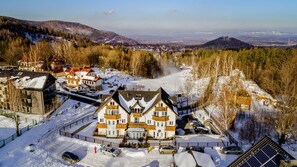 A large, multi-story building with a traditional architectural style, surrounded by snow-covered streets and a mountainous backdrop. - Apartamenty Sun & Snow na Wilczej (Karpacz)