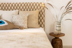 A bed with a woven headboard, a crocheted pillow, and a small wooden side table with a vase and decorative items.