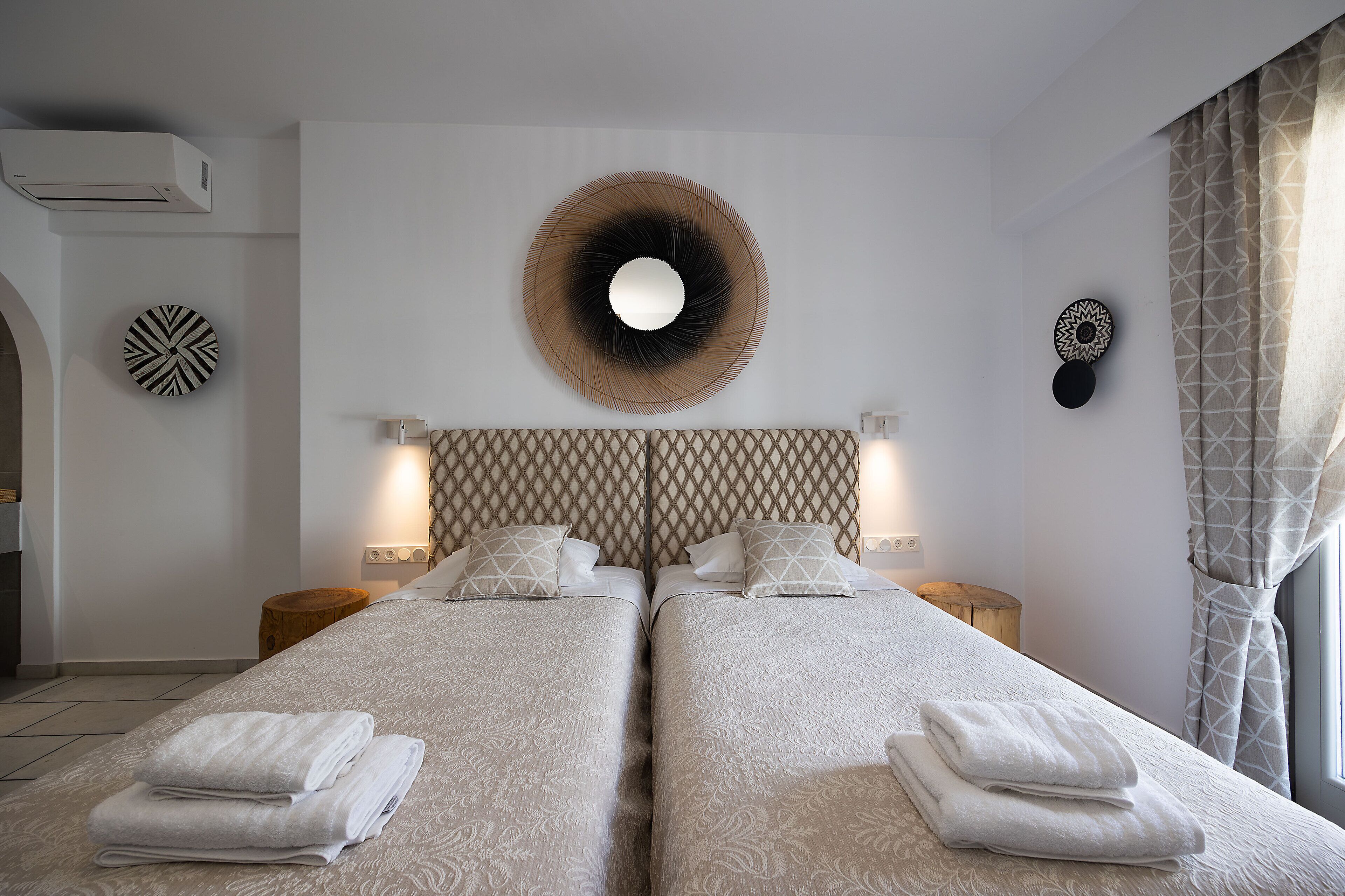 Une chambre d’hôtel avec deux lits, un grand miroir mural et une tête de lit à motifs.