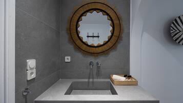 Un baño moderno con un espejo grande, un lavamanos rectangular y una pequeña cesta de mimbre sobre la encimera.