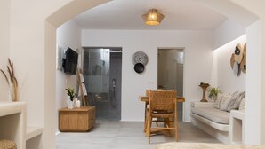Una sala de estar moderna con un sofá, una mesa de comedor con sillas, un televisor montado en la pared y un mueble bajo.