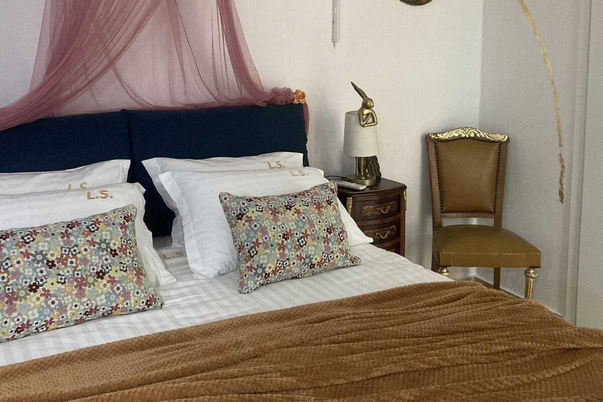 A neatly made bed with a canopy, a decorative lamp, and a chair.