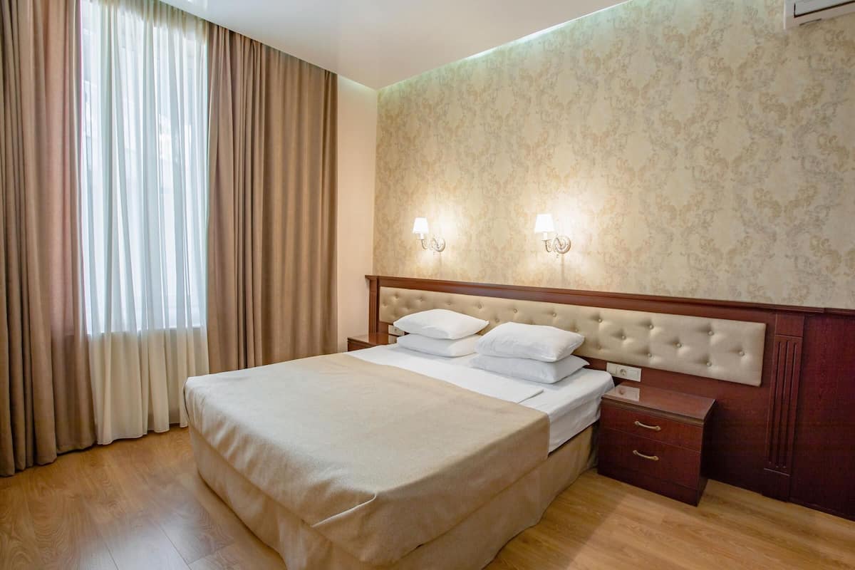 Habitación de hotel con una cama grande, cabecera de madera, dos mesitas de noche y una ventana con cortinas.