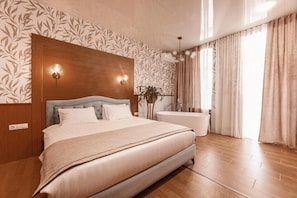 Un dormitorio con una cama, cabecera de madera, lámpara de pared, ventana grande con cortinas y una planta.