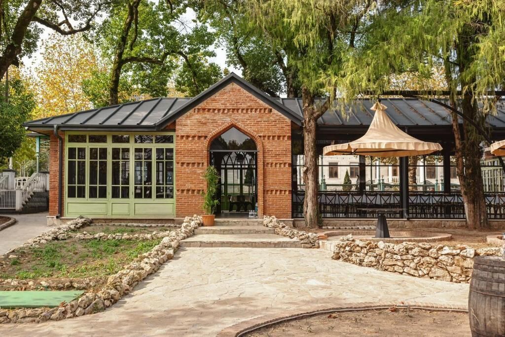 A brick building with a green door and windows, a stone pathway, and a gazebo with a metal roof.