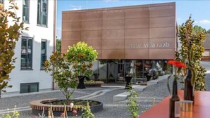 Un hotel moderno con un gran letrero que dice "hotel villa raab" y un patio ajardinado con árboles y una zona de estar circular.