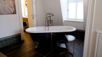 A modern bathroom with a freestanding bathtub, a small round table, and a window providing natural light.