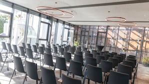 Un salón de conferencias con filas de sillas, ventanas amplias y un diseño moderno en el techo.