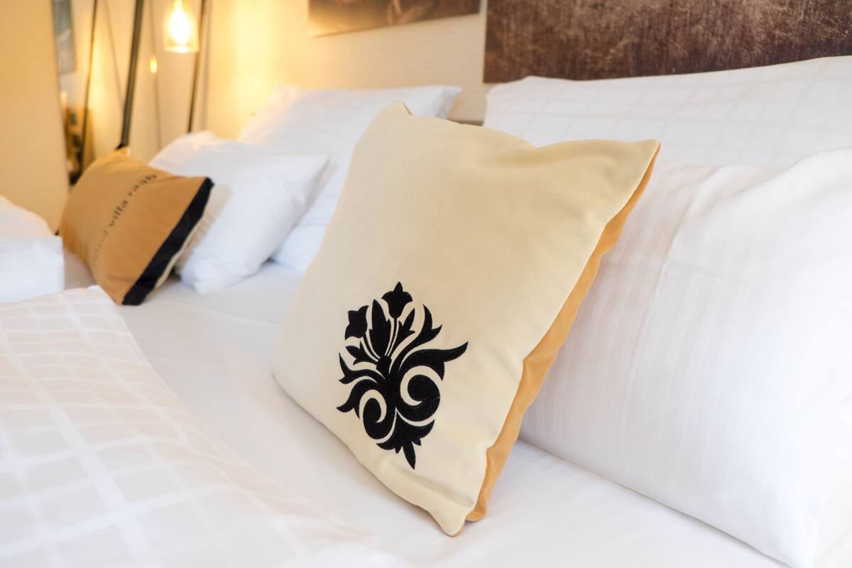Una cama bien hecha con sábanas blancas y un cojín beige con diseño floral negro.