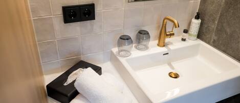 A modern bathroom with a white sink, gold faucet, and a towel rack with folded towels.