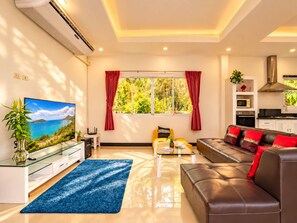 A modern living room with a glass coffee table, a leather sofa, a flat-screen TV, and a large window with red curtains. - Private Pool Villa 4 bedrooms for family (Phuket)