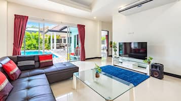Una sala de estar moderna con una mesa de centro de vidrio, un sofá de cuero, un televisor de pantalla plana y vista a una piscina.