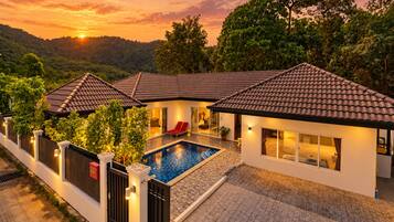 A modern villa with a swimming pool, surrounded by lush greenery and a hilly landscape.