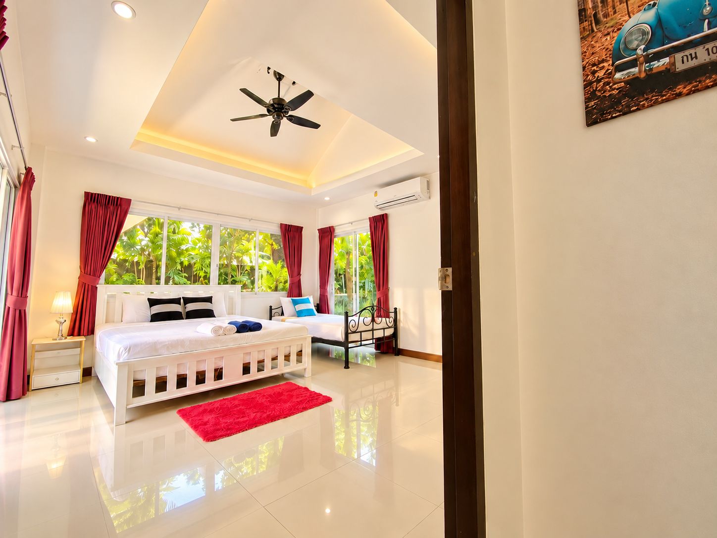 A hotel room with a bed, a red rug, a ceiling fan, and a window with curtains.