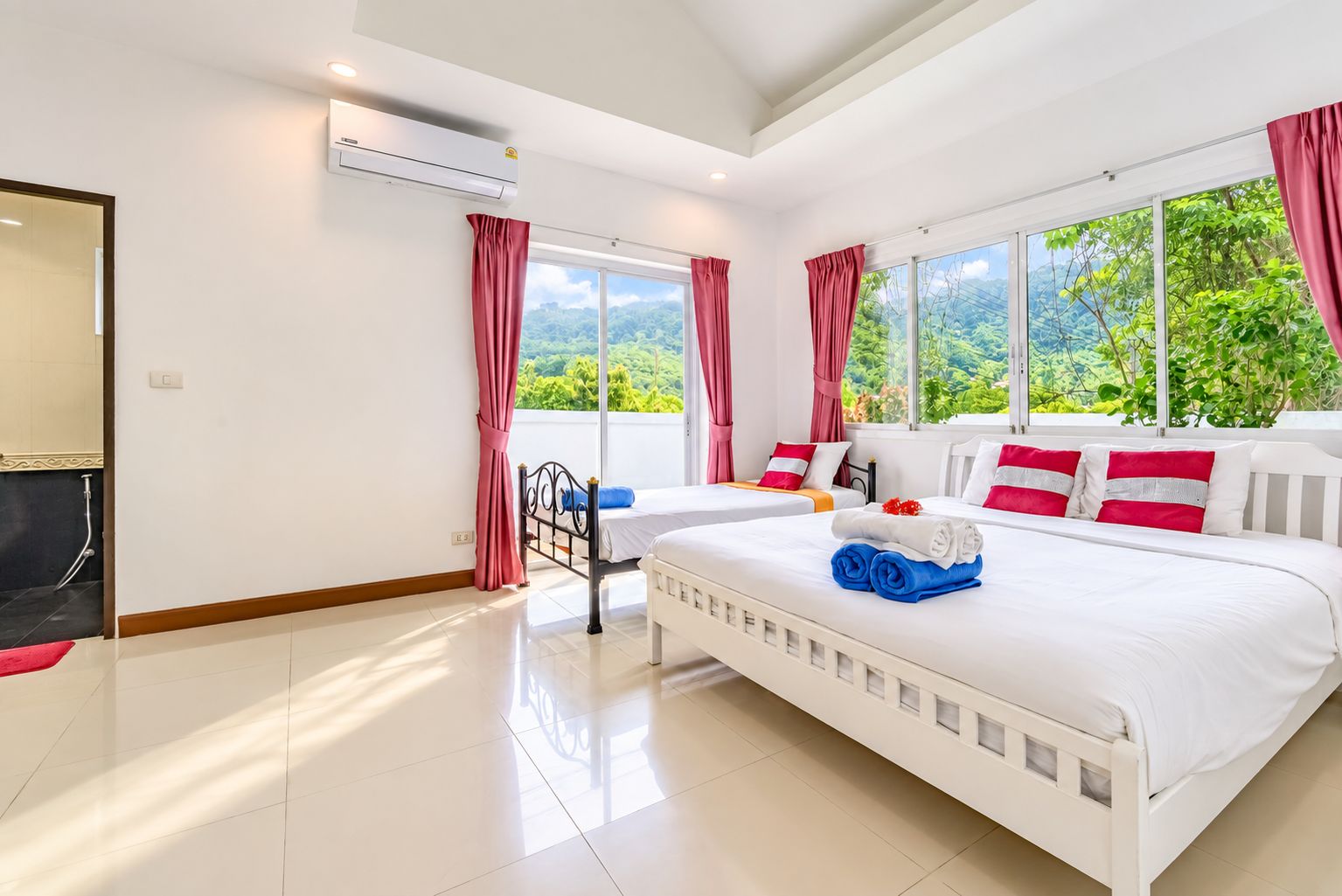 A hotel room with a large bed, two bedside tables, a window with a view of greenery, and an air conditioning unit.