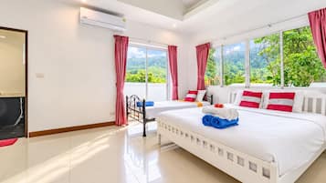 A hotel room with a large bed, two bedside tables, a window with a view of greenery, and an air conditioning unit.