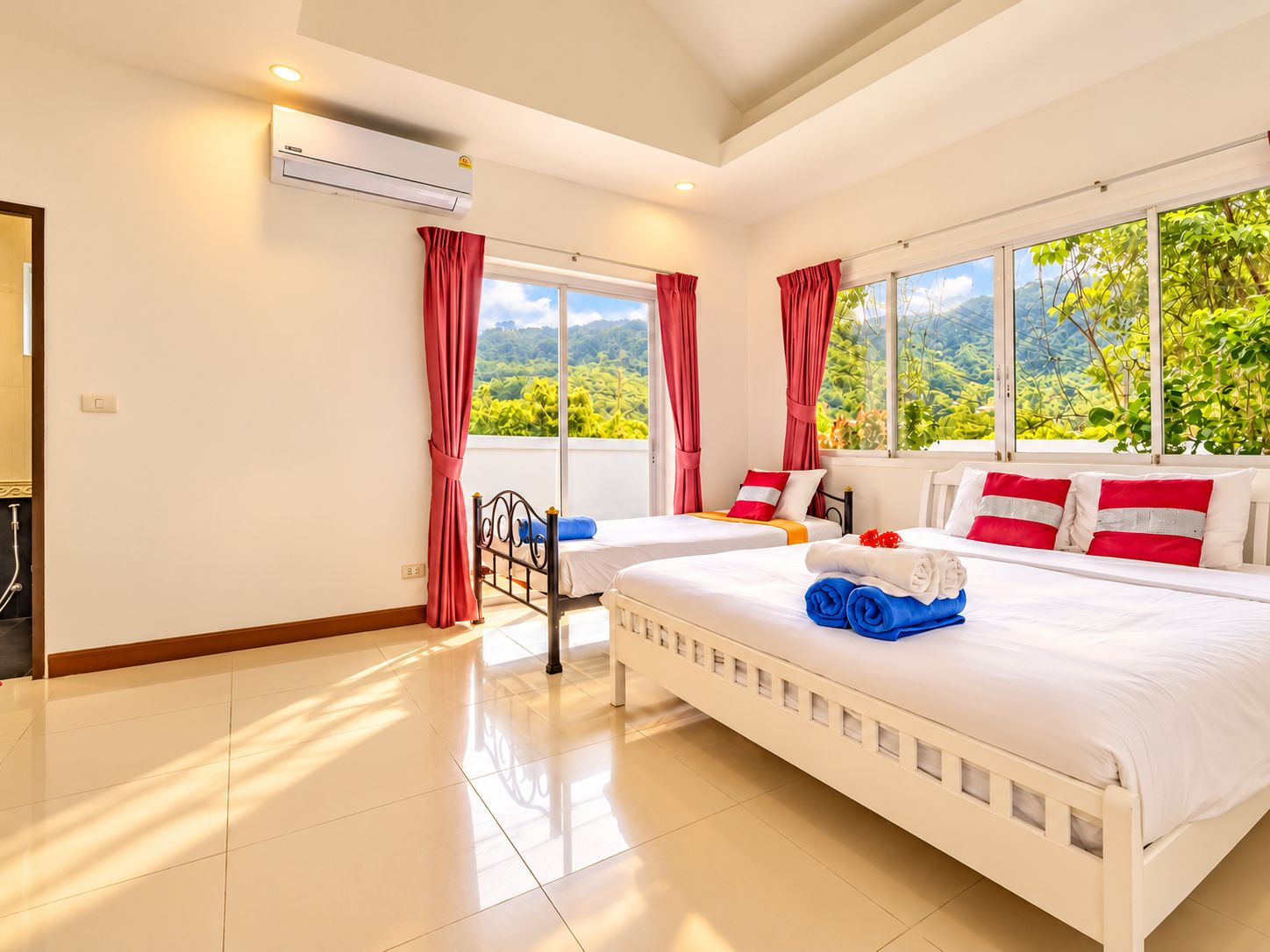 A hotel room with two beds, a window with a view of greenery, and an air conditioning unit.
