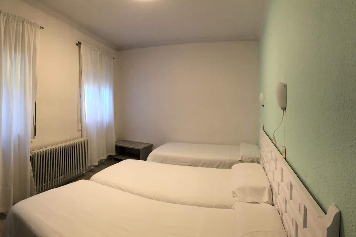 A room with two single beds, a radiator, a small table, and a wall-mounted light fixture.