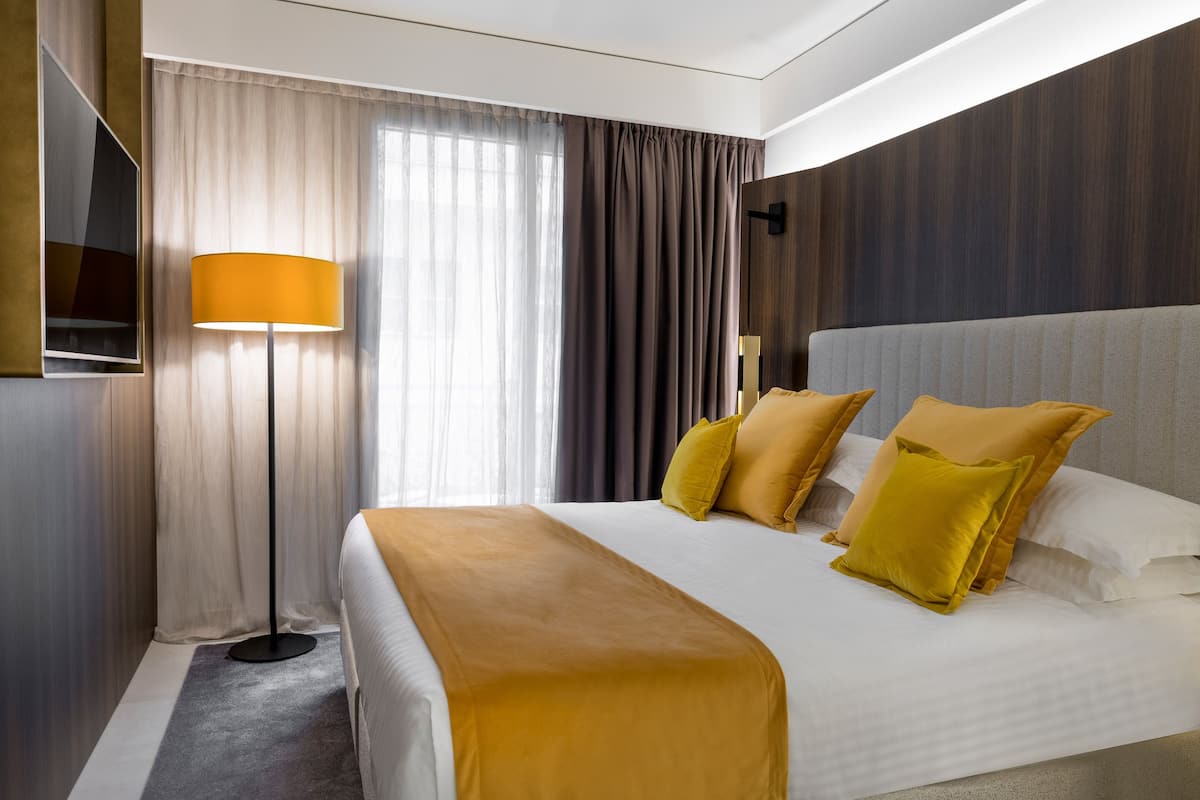 Habitación de hotel con una cama grande, una lámpara de pie y un televisor montado en la pared.
