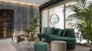 A modern living room with a green sectional sofa, round coffee table, and two ottomans. - We Me Suite Hotel (Riccione)