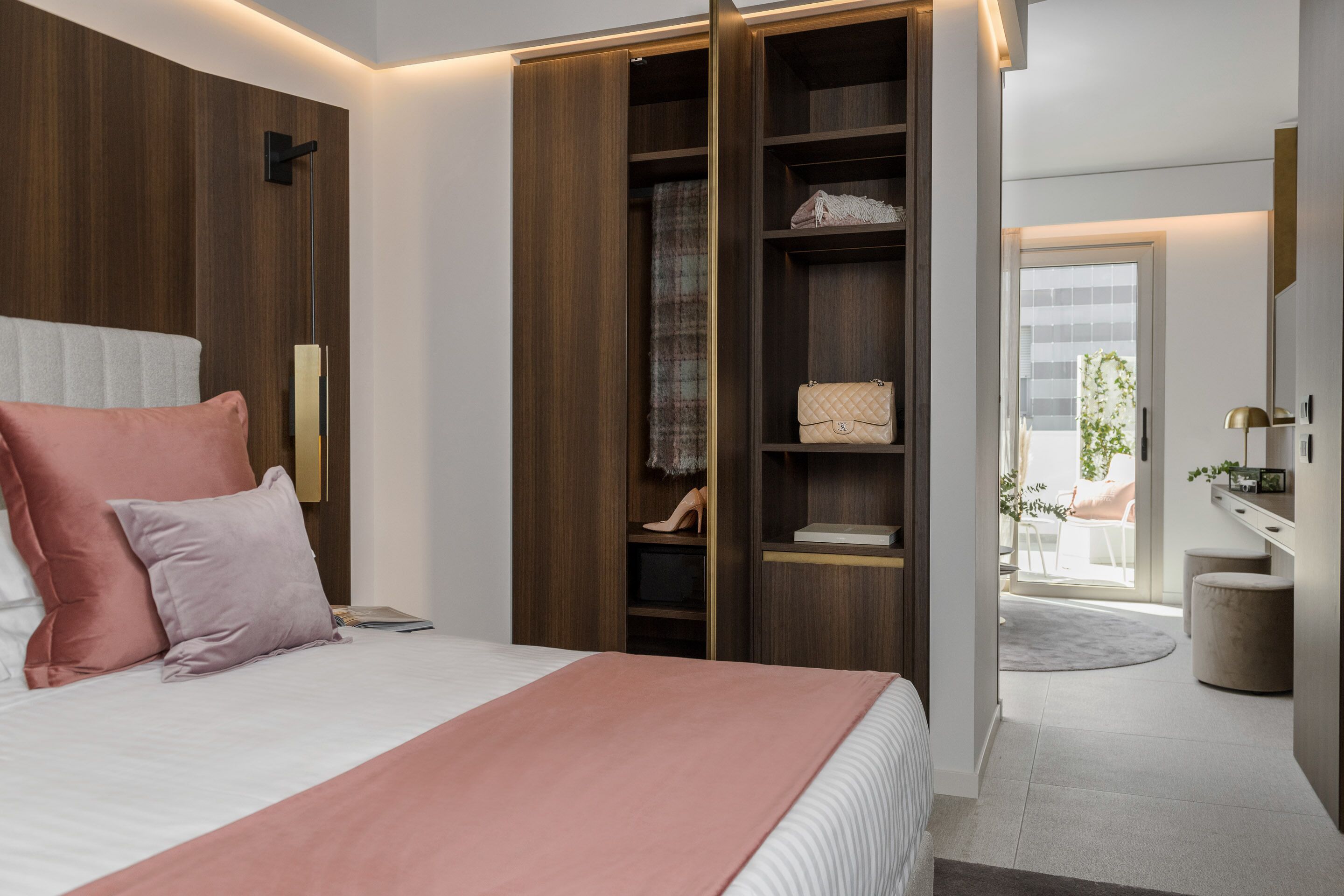 A modern bedroom with a large bed, a wardrobe, and a view of the outdoors.