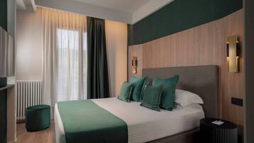 Habitación de hotel moderna con una cama grande, un reposapiés redondo, una mesita de noche y una lámpara fijada a la pared.