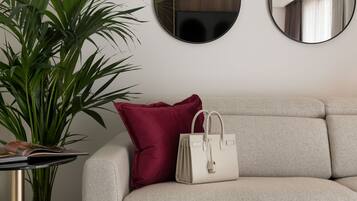 A neutral-toned sofa with a red pillow and a white handbag, a round table with a plant, and two wall-mounted mirrors.