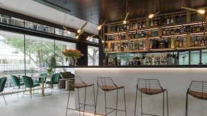A modern bar area with high shelves of liquor bottles, bar stools, and a large window offering a view of the outdoors. - We Me Suite Hotel (Riccione)