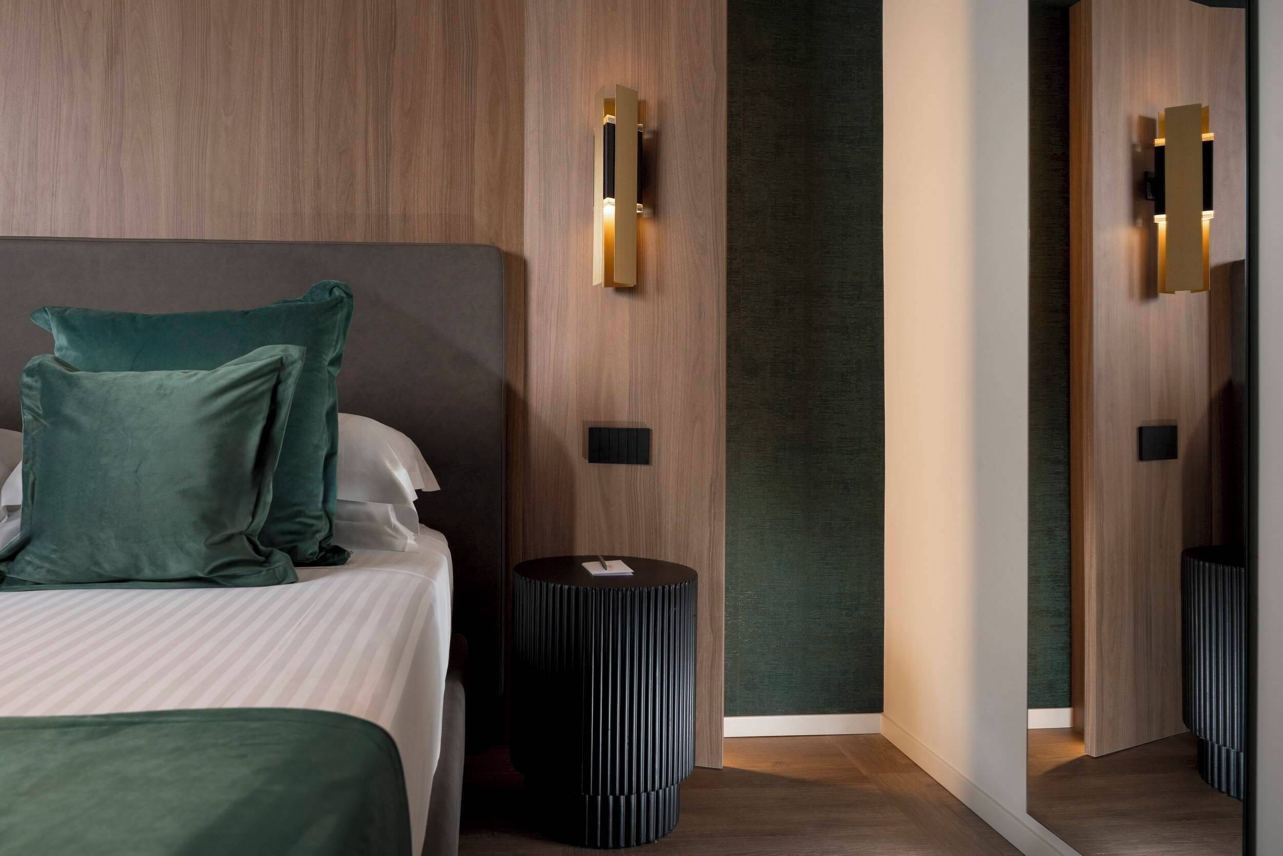 A modern hotel room with a bed, a round side table, and two wall-mounted light fixtures.
