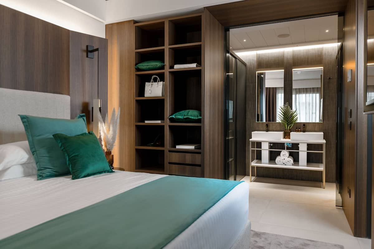 Un dormitorio moderno con una cama grande, un armario empotrado, un tocador con espejo y una pequeña zona de estar.