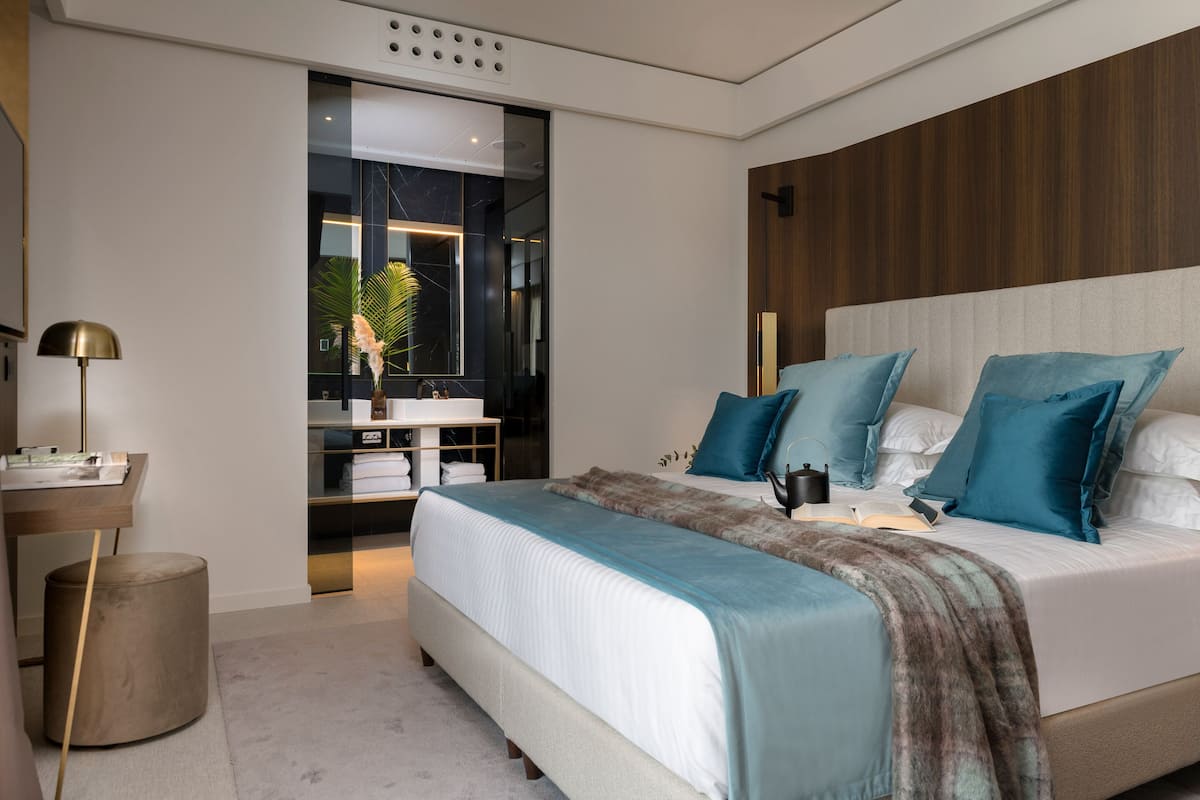 Un dormitorio moderno con una cama grande, una mesita de noche, una lámpara y vistas al baño.