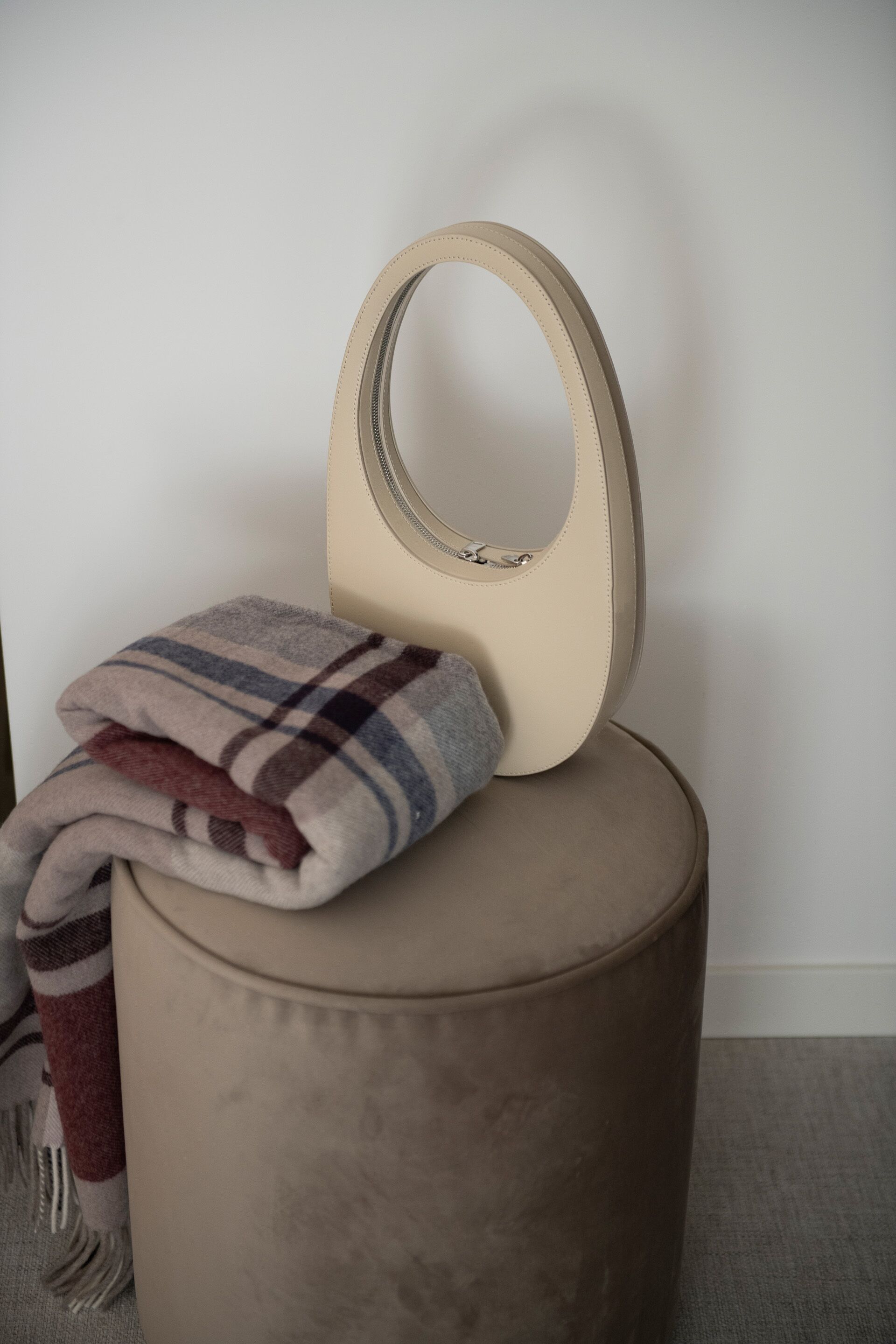 A round ottoman with a beige cushion and a plaid blanket draped over it.