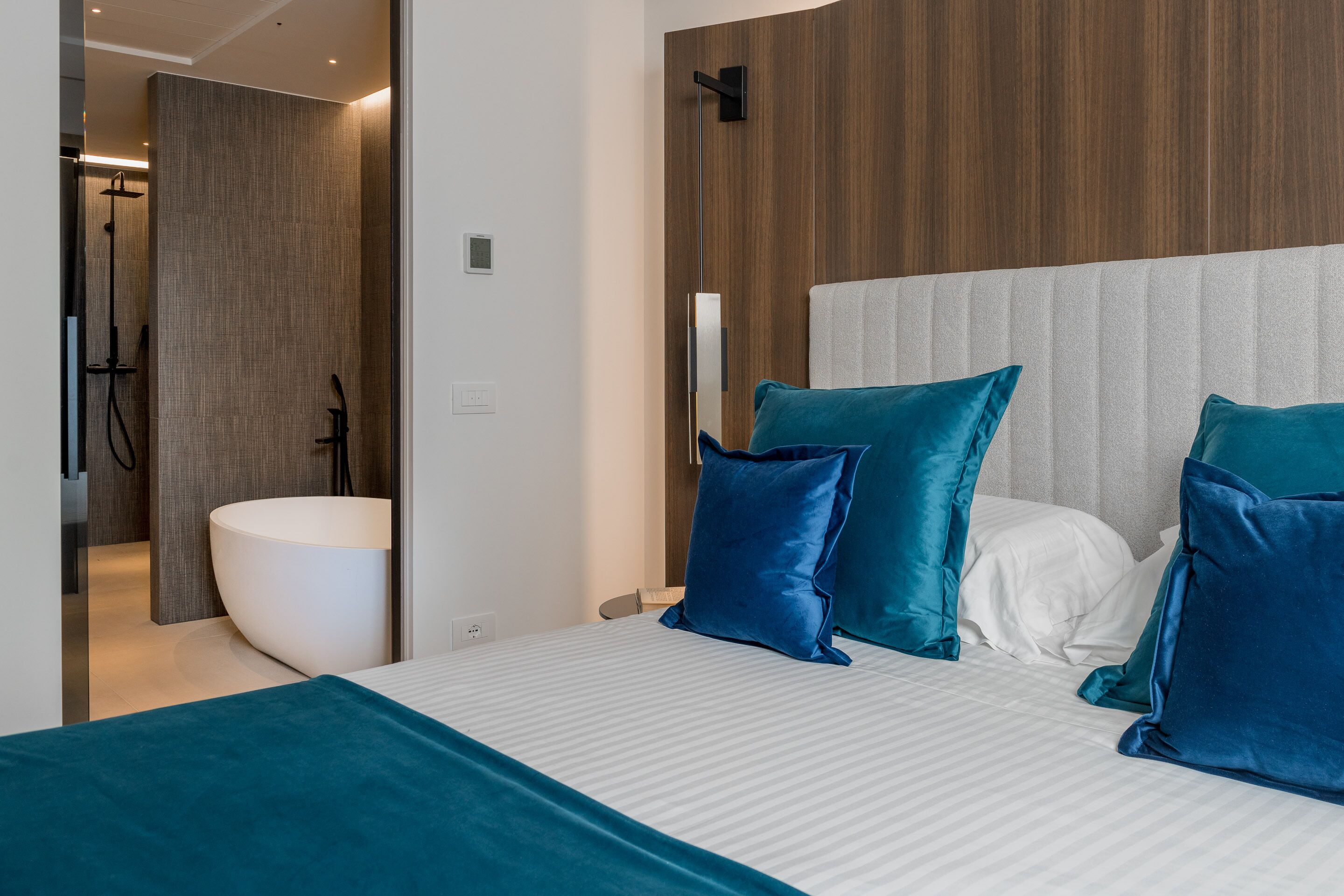 A modern bedroom with a large bed, a headboard, and a bathroom visible through an open door.