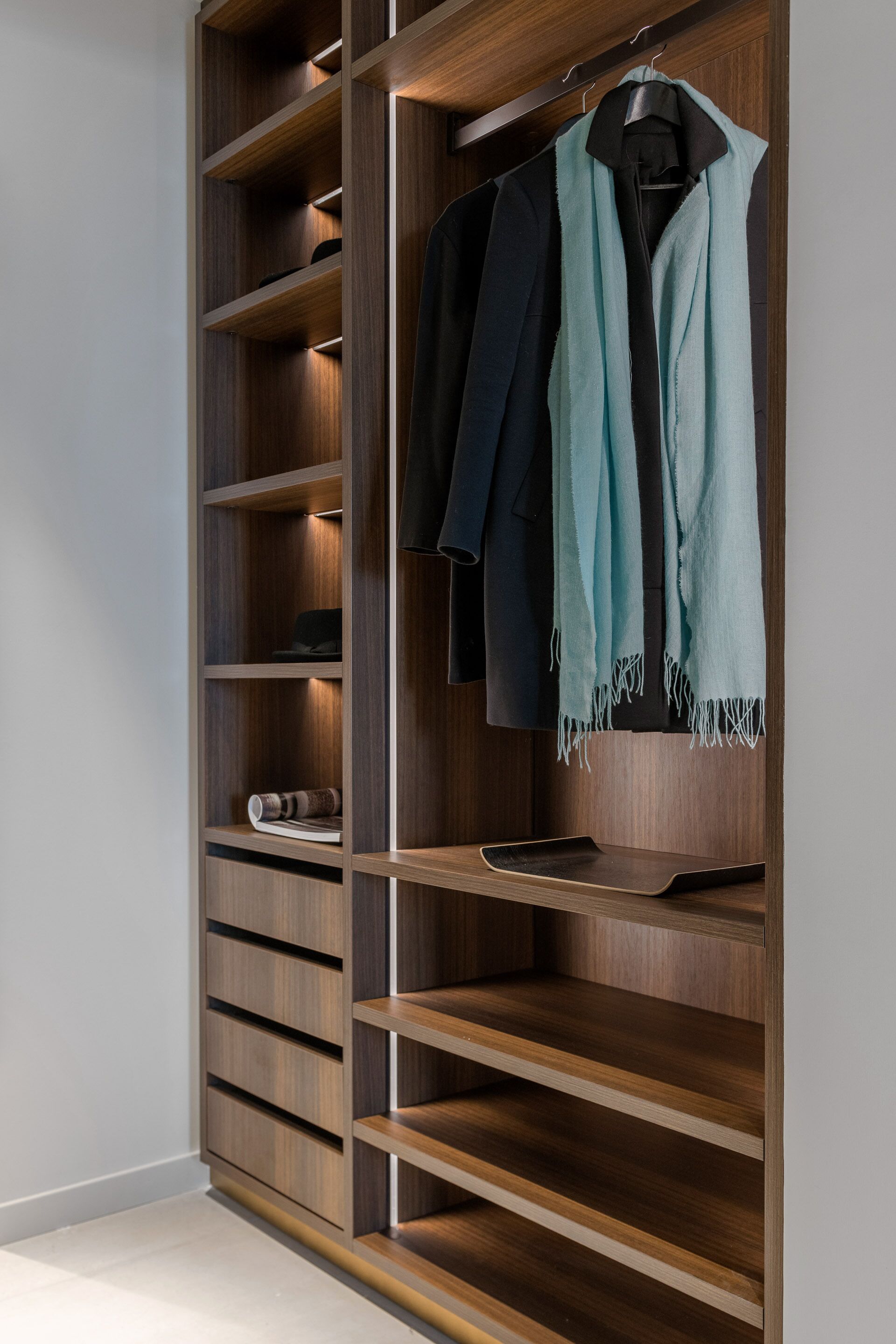 A modern closet with multiple shelves and hanging space, featuring a wooden finish and integrated lighting.