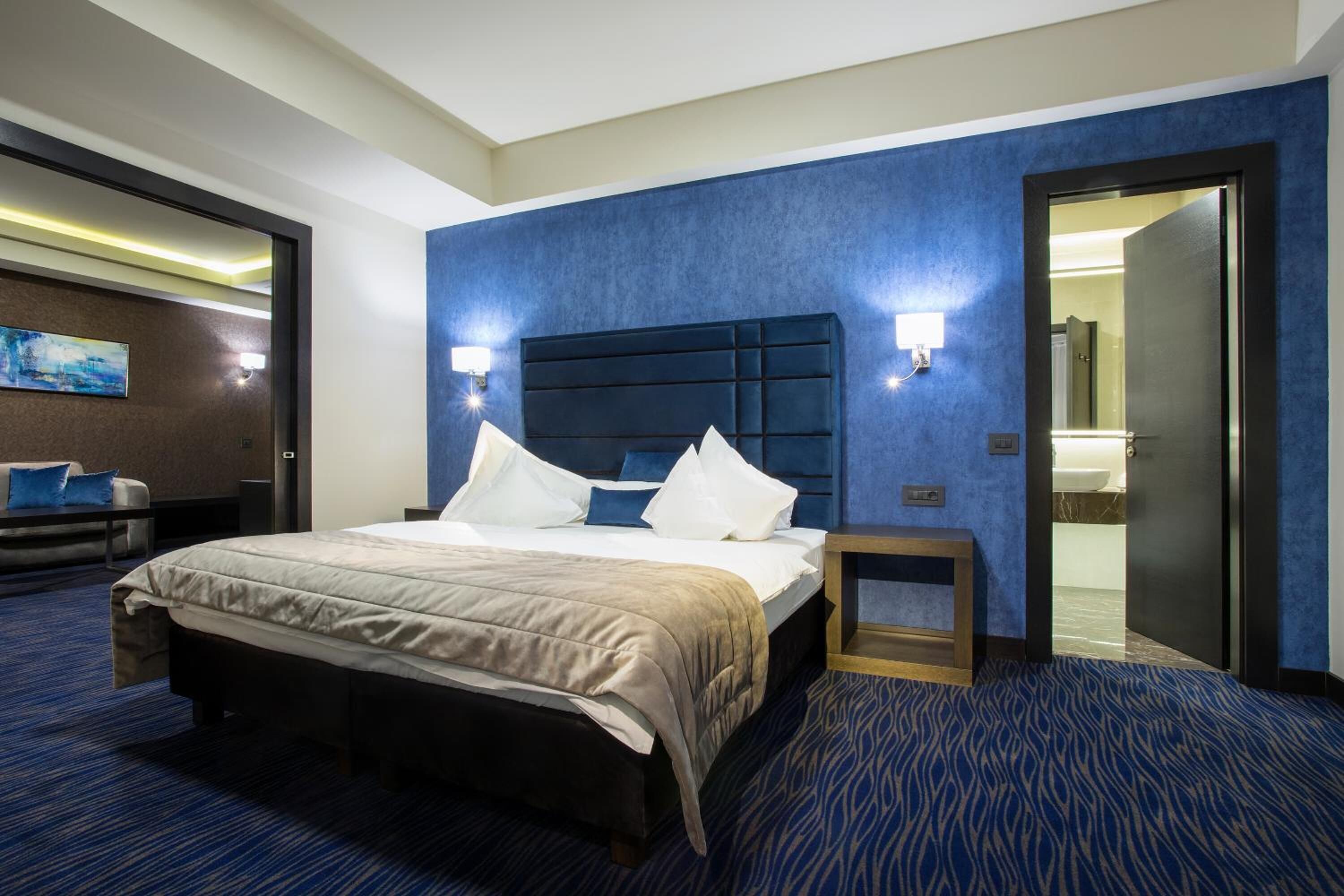 Habitación de hotel con una cama grande, una mesita de noche, una lámpara de pared y una puerta que da al baño.
