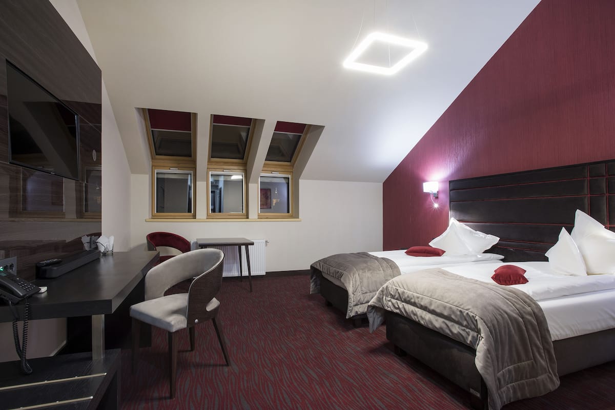 A hotel room with a desk, two beds, a chair, and a large window.