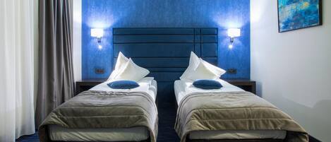 Una habitación de hotel con dos camas individuales, cabecera azul y un cuadro en la pared.