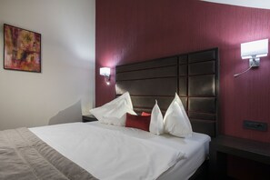 A hotel room with a large bed, a headboard with a panel design, a nightstand with a lamp, and a painting on the wall. - Old Town Hotel (Timisoara)