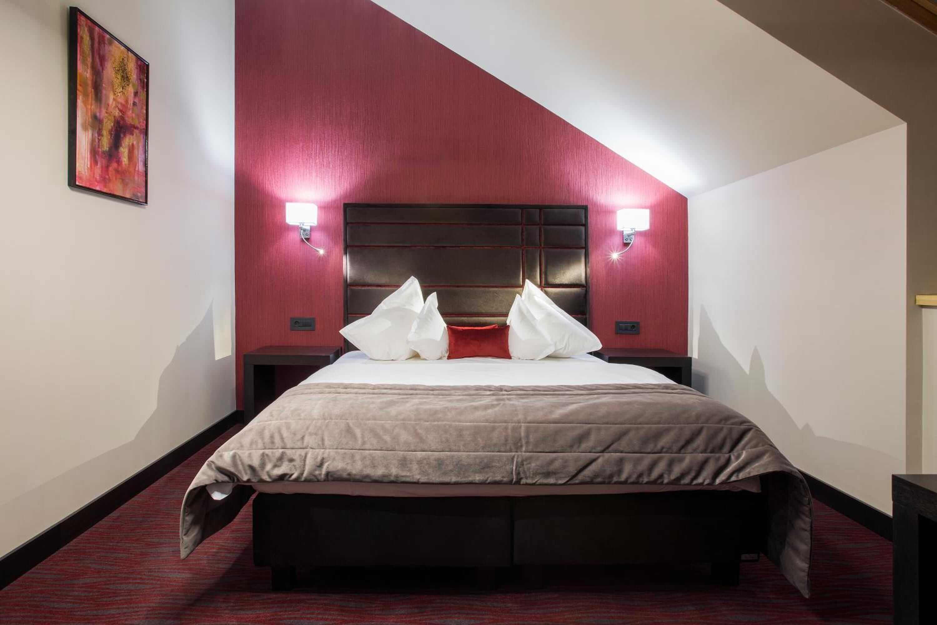A hotel room with a large bed, red walls, and two bedside lamps.