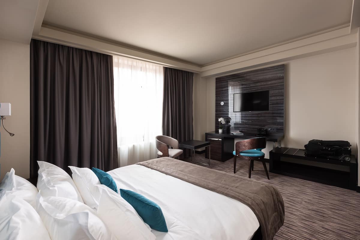 A hotel room with a bed, a desk, a chair, a TV, and a suitcase.